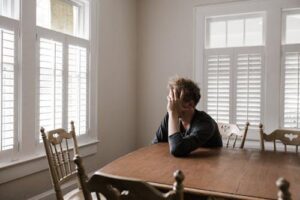 A man sitting alone at a table, reflecting on personal challenges during PSB recovery and managing shame.
