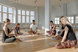 A group of people are sitting barefoot on a wooden floor in a circle, engaging in group discussion