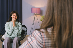 A cheerful young woman smiles while speaking to a psychologist in a modern office with natural lighting.