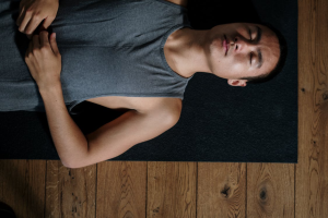 A man in a gray tank top lies quietly on a black carpet.