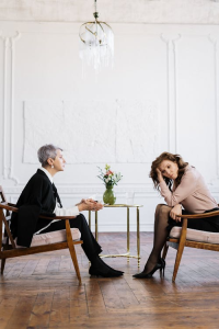 A man and woman sitting side by side on wooden chairs having a conversation.