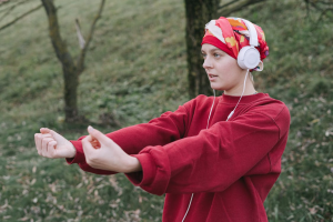 A woman in a red sweater wears white headphones while listening to music.