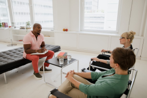Two women are sitting in a therapy session, one speaking and the other listening attentively.