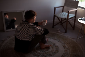 An image of a man sitting on the floor and looking out the window