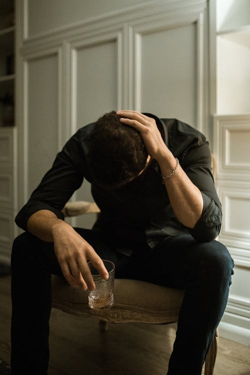 An image of a man holding a glass, looking down in shame