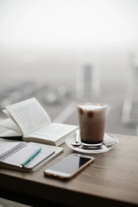 An image of a journal, phone, coffee and a book