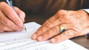 Person signing a document on paper at a desk.