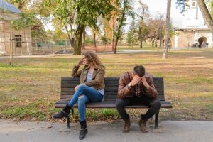 Man and woman sitting together on a wooden bench outdoors.