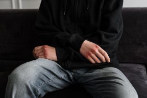 Person wearing a black jacket and blue jeans sitting alone on a black couch indoors